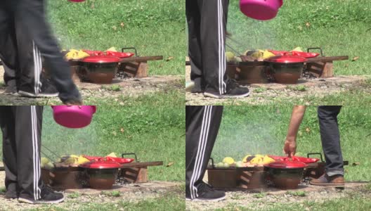 在一个锡盘下面临时搭建的火，上面烤着辣椒，洋葱和肉，一个人用钳子转动着，其他人从他身边经过高清在线视频素材下载
