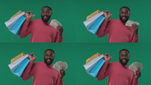 非裔美国人，拿着五颜六色的购物袋和钞票。销售，快乐购物，在一个绿色背景的工作室高清在线视频素材下载