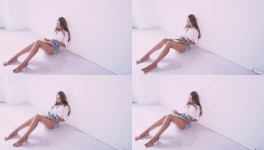 美丽的女孩坐在地板上在一个白色的房间里读书高清在线视频素材下载
