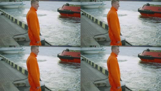 身穿橙色制服的年轻港口工人向正在驶离的轮船挥手高清在线视频素材下载
