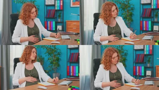 孕妇坐在公司办公桌的椅子上，做笔记，为新客户准备提案，记下公司预算的想法，抚摸着肚子，想着她的孩子高清在线视频素材下载