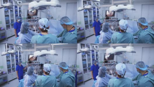 现代手术室的外科手术。身着医疗制服的医生看着屏幕上的手术过程。高科技操作。后视图。高清在线视频素材下载
