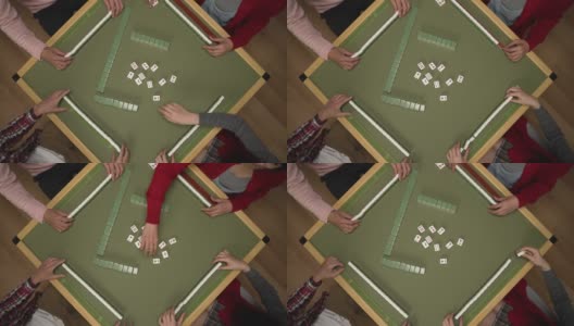 从上面看，人们的手采摘和铺在桌子上的绿色麻将牌，而玩瓷砖游戏在中国春节假期期间在家里高清在线视频素材下载