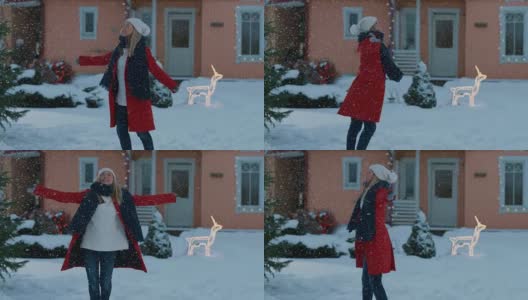 美丽的年轻微笑的女人在飘落的雪纺纱。在她田园诗般的房子的前院，穿着红外套、围着围巾的女孩正在享受冬天。高清在线视频素材下载
