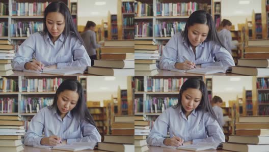 年轻美丽的亚洲女学生坐在桌子周围的书籍在大图书馆重写课本准备考试高清在线视频素材下载