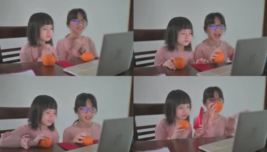 亚洲的中国小女孩和她的妹妹看着笔记本电脑的摄像头，用红包和橘子向她的祖父母祝贺春节高清在线视频素材下载