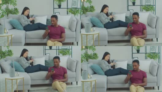 年轻的跨国情侣，无视对方看手机。男人和女人躺在沙发上用着智能手机。高清在线视频素材下载