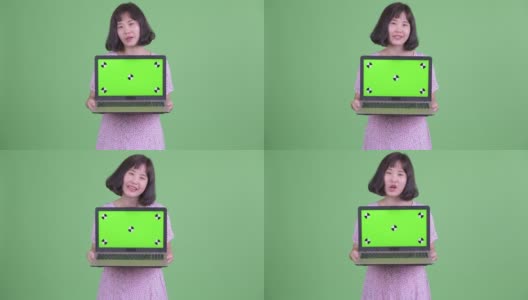 工作室拍摄的美丽怀孕的亚洲女人显示拷贝空间从笔记本电脑在绿色的工作室背景高清在线视频素材下载