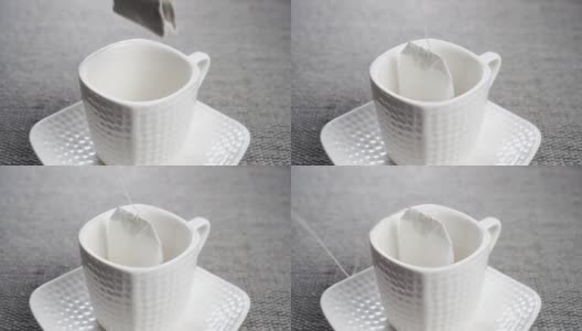 把一个茶包浸入一个白色的空茶杯里，茶托放在一个灰色的有纹理的灰色垫子上高清在线视频素材下载