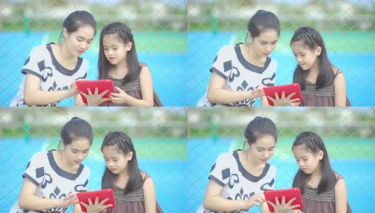 两姐妹坐在操场上一起在iPad上玩游戏。高清在线视频素材下载