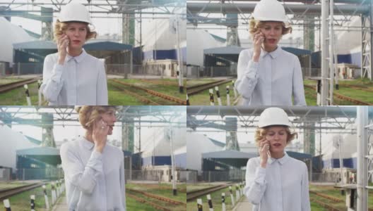 在工业环境中戴安全帽走路和打电话的女人高清在线视频素材下载