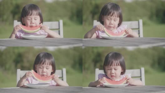 蹒跚学步的小女孩在夏天的家花园里吃西瓜高清在线视频素材下载