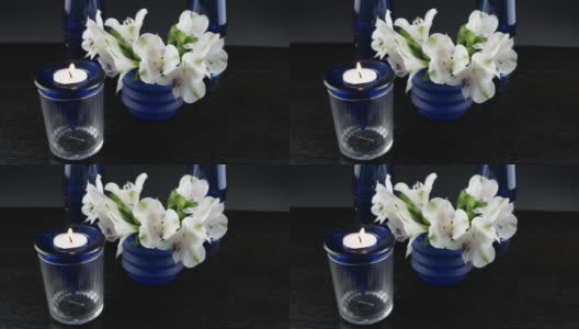 插花:一束白色的花，蓝色的玻璃花瓶和燃烧的蜡烛高清在线视频素材下载