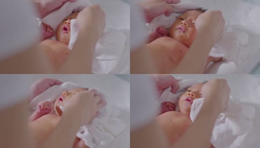 妈妈在宝宝洗完澡后给他盖上毛巾让他干得舒服些。新生婴儿看着她的妈妈用爱擦干她的身体。婴儿新生儿护理和母亲节概念高清在线视频素材下载