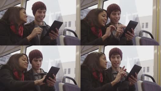 一对年轻夫妇坐在公交车上，一边玩着他们的数码平板电脑一边大笑高清在线视频素材下载