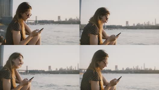 体贴的白人女孩在太阳镜使用智能手机社交网络应用程序，享受惊人的日落在城市海滩4K高清在线视频素材下载