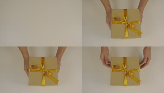 手上伸着一个礼盒，用金色的丝带系着一个蝴蝶结。送礼物。手捧礼盒祝贺某人的节日。赠送礼物。纸板箱是灰棕色的。高清在线视频素材下载