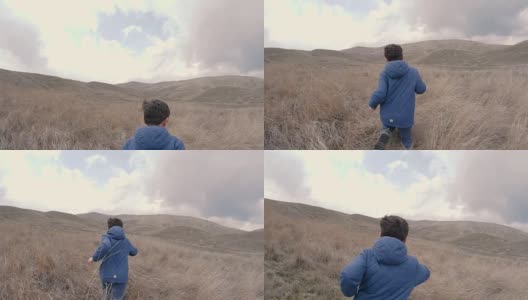 一个在长着高草的场地上的男孩跑到有山的地平线上。慢动作视频高清在线视频素材下载