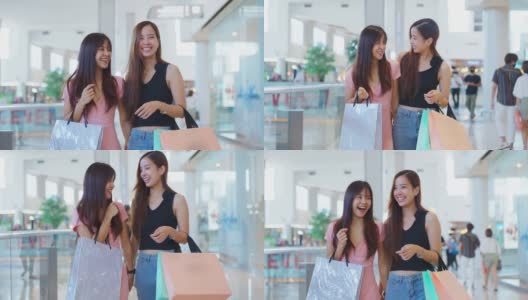 两个快乐的亚洲年轻女性在商场室内购物在销售季节在年底。女孩们拿着购物袋，快乐地走着，微笑着一起买东西高清在线视频素材下载