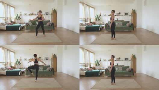 一个年轻的印度女芭蕾舞演员在家里训练，在明亮舒适的房间里做动感运动，穿着黑色上衣和打底裤。运动理念健康生活高清在线视频素材下载