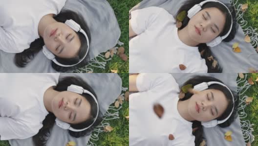 美丽的年轻亚洲女性戴着太阳镜和耳机睡在草地上。高清在线视频素材下载
