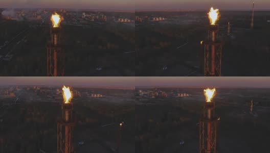 夕阳西下时，树林中炼油厂上的一座塔上挂着火炬。鸟瞰图高清在线视频素材下载