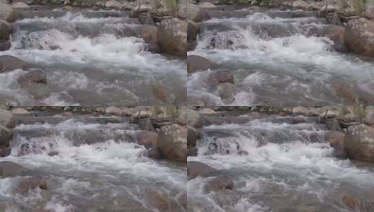 山间的河水从巨石上奔流而下。湍急的水流搅动水流，溅起水花。石质河床。透过透明的表面可以看到花岗岩底部高清在线视频素材下载