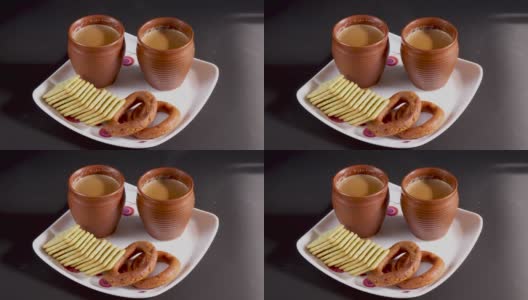 在印度，茶歇期间，用小豆蔻、丁香、姜和肉桂等配料在土制杯子中调制的热马沙拉茶，宵夜放在方形盘子上。高清在线视频素材下载