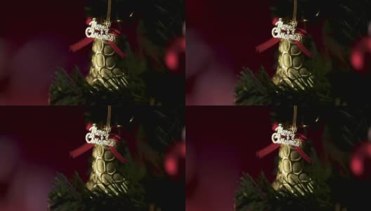 圣诞祝福的话语，金色的装饰铃铛挂在松树枝上，壁炉的火焰在模糊的背景中。圣诞装饰的想法和快乐的年底。高清在线视频素材下载