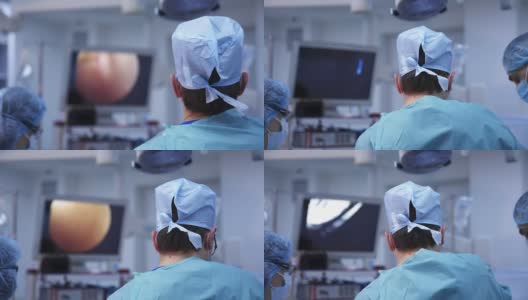 医生们在手术室里使用现代化的医疗设备。外科医生进行手术，并在监视器的屏幕上观察整个过程。后面的观点。高清在线视频素材下载