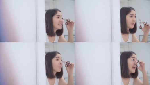 美丽的亚洲女人使用睫毛卷化妆前镜，快乐的女性使用美容化妆品提高自己准备在卧室在家里工作。生活方式女性在家放松的概念。高清在线视频素材下载