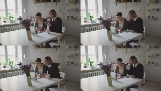 两个女性朋友坐在桌子边用笔记本打发闲暇时光高清在线视频素材下载