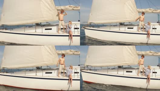 一对年轻的恋人坐在帆船的饲料上，在海水中洗腿高清在线视频素材下载