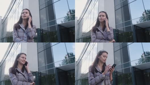 一个穿着休闲服的年轻女孩站在商业中心的背景上，手里拿着一部现代手机。商务女性在她的智能手机上输入信息。办公室附近的电话沟通高清在线视频素材下载