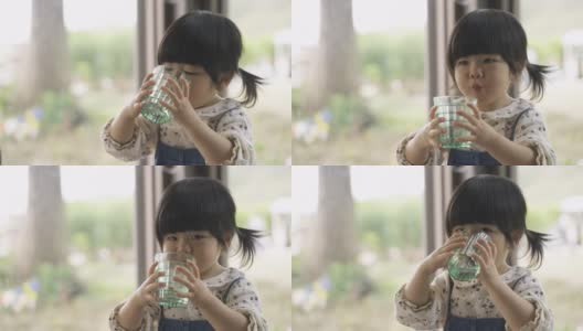 一个口渴顽皮的亚洲小女孩在模糊的玻璃窗户背景下从杯子里流口水和吐水的肖像。高清在线视频素材下载