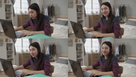 这是在现代风格的卧室里，坐在书桌前的电脑上学习的亚裔女大学生开心地看着镜头的照片。高清在线视频素材下载