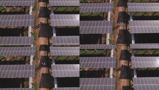 鸟瞰图，工程师和技术人员沿着小线在太阳能电池板农场，电力，太阳能产生的清洁能源之间行走高清在线视频素材下载