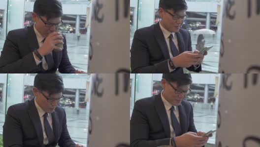 亚洲商人办公室职员坐在咖啡店的窗口边喝咖啡，使用智能手机和互联网在线工作公司业务或短信。商业和技术概念。高清在线视频素材下载