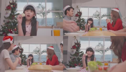 亚洲小孩在家与父母一起享受圣诞派对。有吸引力的漂亮夫妇在餐桌上为年轻的女儿提供晚餐，庆祝圣诞晚会在家里。高清在线视频素材下载