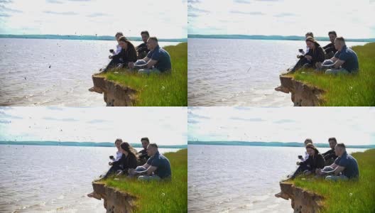 年轻的朋友们坐在河边的小山上享受大自然的周末高清在线视频素材下载