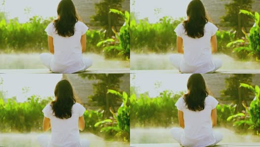 亚洲女孩锻炼瑜伽旁边的健康水疗池在绿色的背景和晨雾的慢动作拍摄高清在线视频素材下载