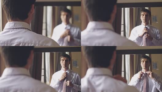 一名穿着白衬衫的英俊男子站在镜子前系着领带。将目光从人转向镜子。3840 x2160高清在线视频素材下载