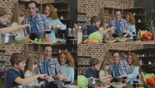 快乐家庭在厨房做饭时使用数字平板触摸屏父母和两个孩子在家交谈高清在线视频素材下载