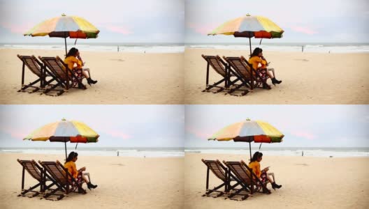 一名年轻女子坐在卡兰古特海滩的躺椅上，正在使用智能手机高清在线视频素材下载
