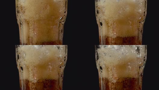 黑色背景上的可乐泡沫与冰块和泡沫玻璃的特写。高清在线视频素材下载