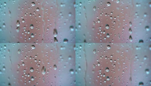 大雨滴落在玻璃窗的背景上。在雨天，水滴在玻璃上流动的慢动作。微距镜头。高清在线视频素材下载