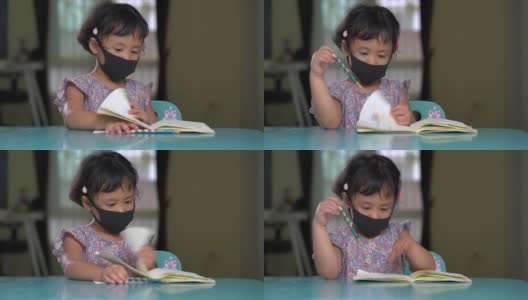 亚洲小女孩戴着防护口罩，在餐桌上专心读书。高清在线视频素材下载