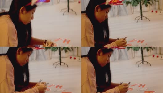 快乐的亚洲女孩戴着红色的驯鹿发带，准备在家里的圣诞树附近的彩旗，生活理念。高清在线视频素材下载