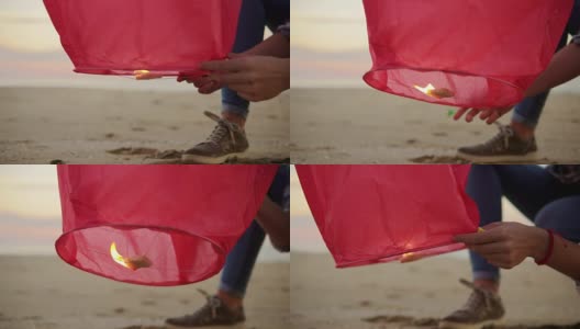 特写手闪电前推出红色纸灯笼。女人们手捧灯笼，举着火，站在海滩前让它飞高清在线视频素材下载