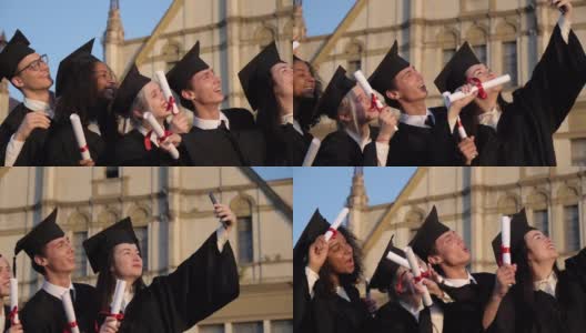 毕业的混血儿们穿着黑色传统长袍，戴着帽子，在智能手机上自拍高清在线视频素材下载